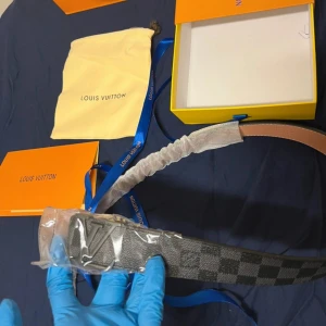 Rutmönstrat bälte  - Säljer ett exklusivt bälte med klassiskt rutmönster i svart och grått. Bältet har ett stort spänne i silver och insidan är i ljust skinn. Perfekt accessoar för att lyfta din outfit.