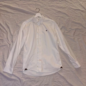 Vit skjorta från Morris med broderi - Vit skjorta från Morris i storlek M, i bomull. Klassisk button-down krage och snyggt mörkblått broderat emblem på bröstet. Passar inte mig längre så säljer den vidare.