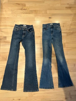 Blå bootcut jeans från Gina Tricot -  Perfect Jeans - Säljer ett par blå bootcut jeans från Perfect Jeans i storlek 34 och XS i fint skick i exakt samma storlek. Jeansen har klassisk femficksdesign, stretch och utsvängda ben. Materialet är jeans med snygga kontrastsömmar och läderpatch bak i midjan. Perfekta för dig som gillar retrovibbar och vill ha en tidlös look. Ljusare paret har litet hål på knäet, vanligt slitage. Ser dock snyggt ut. Priset avser båda paren.