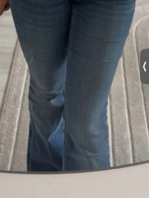 Blå bootcut jeans - Säljer ett par klassiska blå jeans med bootcut-modell. Jeansen har en snygg passform som sitter tajt över låren och släpper ut nedtill. Perfekta till sneakers eller boots och ger en retrovibe till outfiten. Materialet är jeans i bomull och färgen är mellanblå.