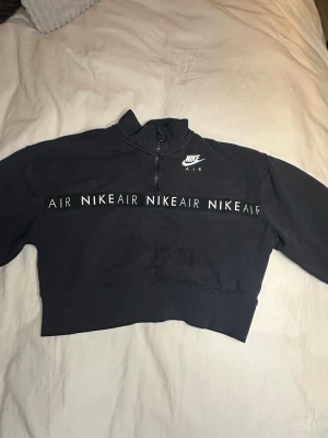 Svart croppad Nike Air half zip tröja - Säljer en svart croppad Nike Air tröja i storlek XS. Tröjan har half zip med ringdetalj, hög krage och tryckt Nike Air-logga samt textband över bröstet. 