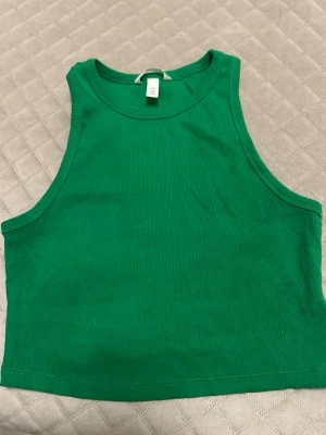 Grön ribbad linnetopp från H&M - Säljer en grön croppad linnetopp från H&M i storlek M. Toppen är ribbad och ärmlös med rund halsringning. Perfekt till sommaren och enkel att matcha med jeans eller kjol.
