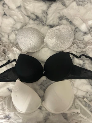Tre BH:ar från H&M, svart och vita - Säljer tre BH:ar från H&M i storlek 75C. En svart och två vita, varav en vit har spetsdetaljer och blommigt mönster. Alla har justerbara axelband och vadderade kupor för extra stöd. Perfekta under alla typer av toppar.