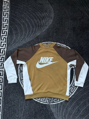 Nike brun och vit sweatshirt M - Denna bruna och vita Nike-sweatshirt har raglanärmar en stor logotyp på bröstet och en liten dragkedja i sidan.