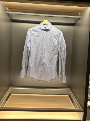 Ljusblå skjorta Tiger of Sweden - Säljer en ljusblå skjorta från Tiger of Sweden i slim fit. Skjortan har klassisk krage, långa ärmar och knappar framtill. Tillverkad i bomull för en skön känsla och stilren look. Perfekt till jeans eller chinos.