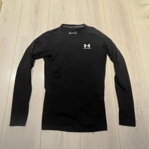 Under Armour kompressiontröja - Säljer nu denna svarta långärmade kompressionströja från Under Armour med HeatGear-teknologi. Tröjan har en liten vit UA-logga på bröstet och är tillverkad i ett stretchigt syntetmaterial som andas. Mycket bra skick, Perfekt för träning! Vid intresse bara att höra av sig! 