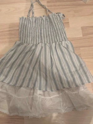 Randig sommartopp med volang - Söt topp med smala axelband och volangkant. Klänningen har blå och vita ränder, smock upptill och ett lager av vitt tyg under för extra volym. 