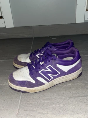 New Balance 480 - Säljer ett par feta New Balance sneakers i lila och vitt. Skorna har klassisk snörning, perforerad tå och den ikoniska N-loggan på sidan. Ovandelen är i mocka och syntet, och sulan är platt för skön vardagsstil. Perfekta för dig som vill sticka ut med färg!