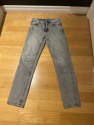 Grå jeans från Nudie Jeans, 27/32 - Säljer ett par gråa jeans från Nudie Jeans i storlek 27/32. Klassisk femficksmodell med raka ben och svarta sömmar på bakfickorna. Jeansen har en ljus tvätt och är tillverkade i slitstark bomull. Perfekta för en avslappnad och stilren look.