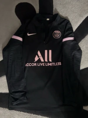 PSG Nike träningströja – svart/rosa, storlek M - Stilren PSG (Paris Saint-Germain) träningströja från Nike i svart med rosa detaljer. Perfekt för träning, fotboll eller vardagsbruk. Tröjan är i mycket bra skick och sparsamt använd. Storlek M, normal passform. Priset kan diskuteras 