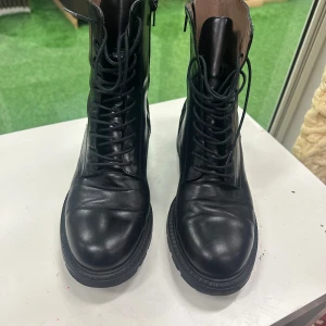 Svarta boots från Wonders i skinn 42 - Snygga svarta boots från Wonders i äkta skinn med snörning framtill och dragkedja på sidan. Grov sula och rund tå ger en cool look. Dekorativa sömmar och detaljer längs kanten. Perfekta för höst och vinter!