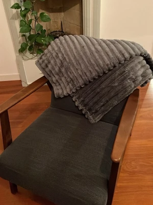 Mörkgrå mjuk och mysig filt i syntet - Säljer en mörkgrå mysig filt i mjukt syntetmaterial med ribbat mönster. Filten är 100x150 cm. Filten ger en riktigt mysig känsla som är perfekt för dig som vill ha något extra mysigt till din fredagskväll.