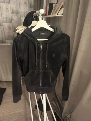 Svart Juicy Couture tröja - Juicy Couture tröja i svart  med dragkedja och huva. Klassisk logga på bröstet och snörning i huvan. Mjuk och skön! Den sitter jätte fint på! Pris kan diskuteras