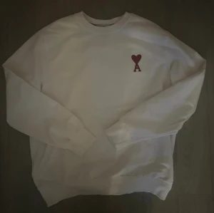  Ami Paris  - Vit sweatshirt från Ami Paris med det ikoniska röda hjärta-A broderiet på bröstet. Klassisk rund halsringning och långa ärmar. Tillverkad i mjuk bomull för en clean och stilren look. Storlek L, helt oanvänd behöver få sålt snabbt till studenten!