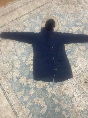 Mörkblå parkas med fuskpäls - Säljer en mörkblå parkas från C med mysig fuskpäls runt huvan och mjukt teddyfoder på insidan. Jackan har dragkedja och knappar framtill samt två stora fickor. Perfekt för kalla dagar och riktigt skön att bära.