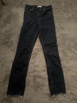 Mörkblå jeans från Perfect Jeans, strl 34 - Säljer ett par mörkblå jeans från Perfect Jeans i rak modell. Klassisk femficksdesign med kontrastsömmar och råa, fransiga benslut för en avslappnad vibe. Tillverkade i slitstarkt denim med dragkedja och knapp framtill. Själv så är jag 176 med långa ben och är lite för korta för mig