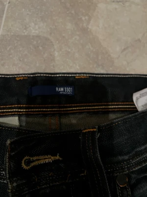 G-Star RAW 3301 svarta jeans - Säljer ett par G-Star RAW 3301 jeans i svart tvätt med slitningar och kontrastsömmar. Klassisk femficksmodell med tryckt logga på fickan och bak. Jeansen har rak passform och är gjorda i slitstarkt denimtyg. Perfekta för en cool och avslappnad stil.