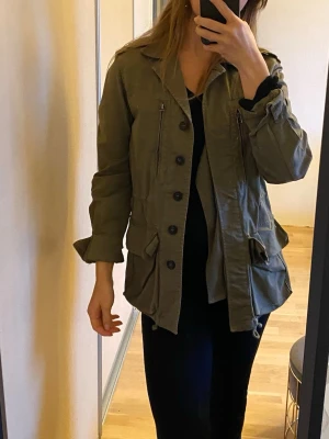 Olivgrön parkajacka från Zara Basic - Mörkgrön ”militärjacka” /vårjacka/sommarjacka/jeansjacka dam Går att dra åt i midja och längs ner, knappar i ärmarna, jackan stängs med knappar. Många fickor  Zara storlek S  Inga större synliga skavanker, jackan har lätt sliten look sedan från början så svårt att säga vad som är slitage och vad som hör till, men den har inga tydliga defekter/fel :)