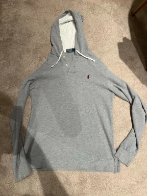 Grå Ralph lauren hoodie  - En grå Ralph lauren hoodie som är i storlek S och i mycket bra skicka. Den är köpt i Italien för cirka 1500kr säljer den för 500kr men kan gå ner i pris vid snabb affär. Skicka om du har någon fråga.