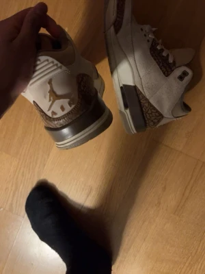 Nike Air Jordan 3 beige/bruna sneakers - Säljer ett par Nike Air Jordan 3 sneakers i beige och brunt med ikoniskt elefantmönster och Jumpman-logga på hälen. Skorna har snörning, rund tå och platt sula. Materialet är en mix av mocka och skinn, vilket ger en schysst premiumkänsla.