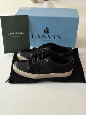 Lanvin - Säljer ett par stilrena Lanvin sneakers i svart, i mycket fint skick. Klassisk och tidlös modell som passar både till vardag och mer uppklädda outfits.  ✔️ 100 % äkta ✔️ Box, kvitto och dust bag ingår ✔️ Väl omhändertagna och sparsamt använda ✔️ Köpta via Care of Carl  Skorna är tillverkade i högkvalitativa material och håller Lanvins välkända lyxkänsla och komfort.