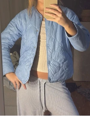 Ljusblå quiltad jacka - Ljusblå quiltad jacka med tryckknappar framtill.