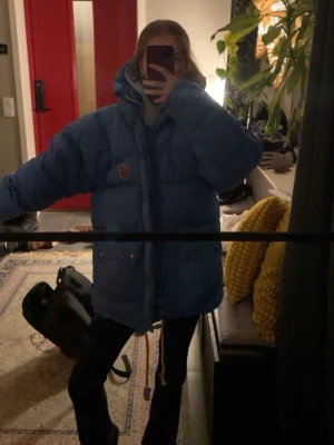 Blå dunjacka från Fjällräven XXS - Säljer en blå, oversized dunjacka från Fjällräven i storlek XXS. Knappt använd, har precis kemtvättat jackan. Skulle säga att den passar XS/M. De vita ”lapparna” på snöret är lite förstörda men inget som syns på långt håll. Ny pris 9 999kr