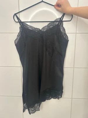 Svart spetslinne med snedskuren kant - Supersnygg svart spetslinne från HM med tunna axelband och en sneskuten spetskant som ger en extra touch. Perfekt att antingen bara ha som en topp eller att ha under kavaj eller tröjor. Helt ny med lappen kvar.