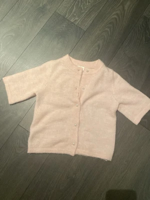 Ljusrosa kofta från Gina Tricot( Young) - Supersöt ljusrosa kofta från Gina Tricot med korta ärmar och pärlknappar framtill. .