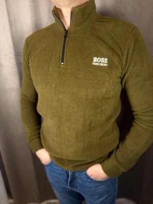 Olivgrön fleece från Hugo Boss - Säljer en olivgrön fleece från Hugo Boss—perfekt för kyliga dagar. Tr Google Translate öjan har hög krage, half zip och broderad cu logo på bröstet. Mjuk och riffad känsla, långärmad och normal pass  ning. Snygg att bära till jeans eller över en t-shirt.