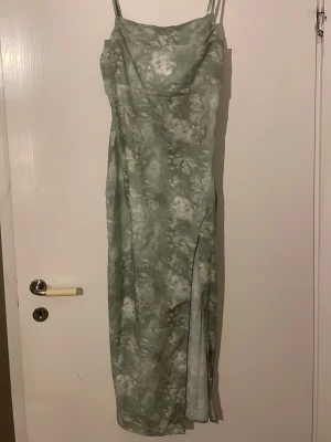 Grön blommig långklänning med slits - Snygg långklänning i ljusgrönt med blommigt mönster och tunna axelband. Klänningen har en slits på sidan som ger en extra touch och är figurnära i modellen. Perfekt för sommarens alla tillfällen. Materialet känns lätt och luftigt. Klänningen är i storlek M och är från Shien. Den är helt oanvänd 