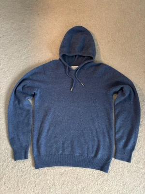 Blå hoodie i merinoull från Ahlquist - Mysig blå hoodie från Ahlquist Clothing i 100% merinoull storlek xxs, L57cm B43cm. Tröjan har huva med snörning och ribbade muddar vid ärmslut och nederkant. Perfekt för dig som vill ha något både snyggt och bekvämt till hösten eller vintern❄️🍂. Nypris är köpt för 999kr använt få gånger.