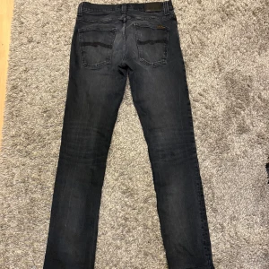 Nudie Jeans Grim Tim  - Mörkgråa nudie jeans i modellen Grim Tim. Storlek w31 l34 sitter som 30/32. Inga defekter utom ett hål i fickan.