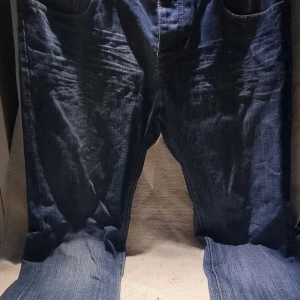 Blå jeans från Beavers, storlek 36 - Säljer ett par klassiska blå jeans från Beavers i storlek 36. Jeansen har rak passform, fem fickor och knappstängning fram. Materialet är slitstarkt denim och färgen är mörkblå med lätt tvättad look. Perfekt för dig som gillar enkel och tidlös stil.