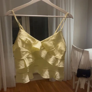 Gul volangtop  - Säljer en ljusgul linnetopp från SHEIN med tunna axelband och flera volanglager. Toppen har en lätt skrynklig struktur och är perfekt för varma dagar. Snygg och luftig modell som ger en somrig vibe.