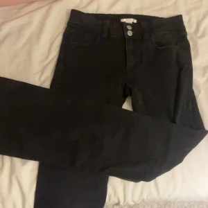 Svarta jeans  - Svarta jeans från Gina Tricot med klassisk femficksdesign och två silverfärgade knappar i midjan. Jeansen har raka ben och diskret broderi på bakfickorna. Materialet är stretchigt jeans för en bekväm passform.