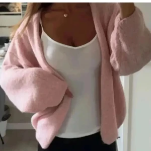 Rosa kofta från Lindex - Mysig rosa kofta från Lindex med oversized passform och långärmade, fluffiga ärmar. Koftan är stickad och har en öppen front utan knappar, perfekt att slänga över en topp. Superfin ljusrosa färg som ger en soft vibe till din outfit.