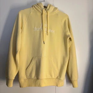Gul hoodie från Peak Performance - Snygg ljusgul hoodie från Peak Performance med broderad logga på bröstet. Tröjan har huva med snörning, känguruficka och ribbade muddar. Snörningen är lite skadad som man kan se på bilden. 
