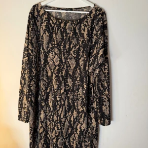 Beige och svart klänning Ilse Jacobsen - Snygg långärmad klänning från Ilse Jacobsen i beige och svart med coolt zebramönster. Modellen är rak och har rund halsringning, perfekt för dig som gillar att sticka ut. Materialet är mjukt och följsamt, vilket gör den superbekväm att bära.