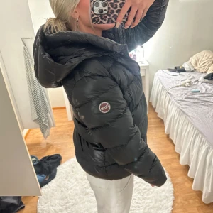 Colmar vinterjacka  - Säljer en svart dunjacka från Colmar med stor, mysig huva och dragkedja framtill. Jackan är vadderad och har en klassisk puffer-look med logga på ärmen. Perfekt för kalla dagar och riktigt snygg till både jeans och mjukisbyxor. 