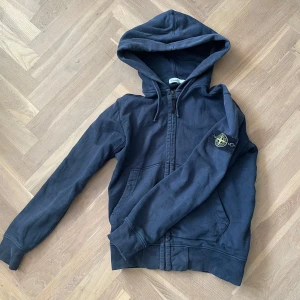Blå Stone Island zip hoodie - En stilren och basic marinblå Stone hoodie.  Ganska använd därav kan pris dirskuteras och som ni ser på bilden finns det ett litet hål på bakre delen ärmen. Skick 5/10. Storlek S. Hör gärna av er vid intresse och information! 🤗