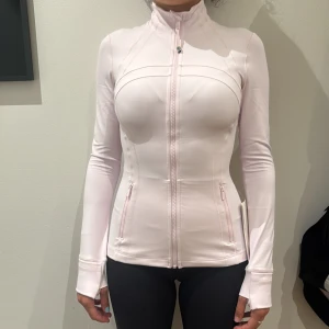 Ljusrosa zip-tröja från Lululemon - SLUTSÅLD!!!Supersnygg ljusrosa långärmad zip-tröja från Lululemon med tight passform. Tröjan har hög krage, dragkedja framtill, praktiska fickor med dragkedja och tumhål vid ärmslut. Perfekt för träning eller chill dagar. Materialet är mjukt och stretchigt syntet. Storlek 4=XS-S