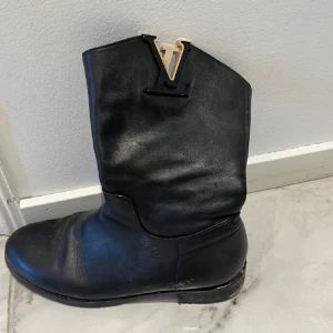 Svarta boots  - Snygga svarta boots med ikonisdetalj upptill. Klassisk rund tå och platt sula, perfekt för dig som vill sticka ut med en lyxig touch. Passar till många olika outfits och ger en exklusiv känsla.