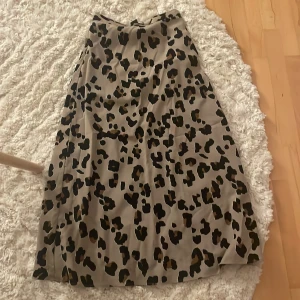 Leopardmönstrad långkjol från Lindex XS - Snygg långkjol från Lindex i beige med leopardmönster i svart och brunt. Kjolen har en rak och flowy passform och är tillverkad i ett mjukt, lätt material som känns skönt mot huden. Perfekt för dig som vill sticka ut med ett trendigt djurmönster.