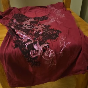 Vinröd topp med blommigt mönster - Snygg vinröd topp med rund halsringning och tryckt blommigt mönster i svart och ljusrosa framtill. Toppen är ärmlös och har en mjuk känsla, perfekt för dig som gillar unika detaljer. Materialet känns som bomull och toppen har en normal passform.