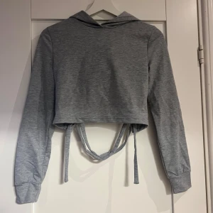 Grå croppad hoodie med snörning SHEIN - Grå croppad hoodie från SHEIN med långa ärmar och cool snörningsdetalj i ryggen. Tröjan har huva och är tillverkad i mjukt material