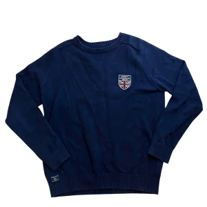 Morris tröja - Mörkblå stickad tröja från Morris med rund halsringning och ribbade muddar. På bröstet sitter en snygg patch med brittisk flagga och Morris-logga. Perfekt för dig som gillar klassisk och stilren look.