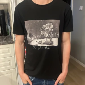 Svart t-shirt med boxningsmotiv - Svart t-shirt med coolt tryck av en klassisk boxningsmatch och texten 'It's Goin' Down' på bröstet. T-shirten har normal passform, rund hals och är kortärmad. Perfekt för dig som gillar sportiga och stilrena plagg.
