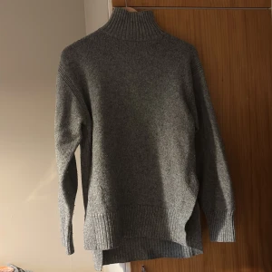 Grå polotröja från H&M XS - Mysig grå polotröja från H&M i stickad kvalitet. Tröjan har hög ribbad krage, långa ärmar och breda ribbade muddar vid ärmslut och nederkant. Den är även snittad längst ned. Perfekt för lager-på-lager under kyliga dagar.