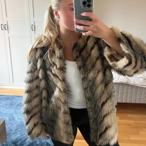 Brun och svart pälsjacka - Säljer en fluffig pälsjacka i bruna och svarta toner med tydliga diagonala ränder. Jackan har en loose passform och långärmad. Materialet är pälsimitation och jackan är riktigt mjuk och varm. Jackan är i storlek L men skulle mer säga att den är en M, jag är 160cm för referens. 